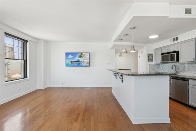 kitchen with gray cabinetry, stainless steel appliances, a kitchen breakfast bar, tasteful backsplash, and pendant lighting