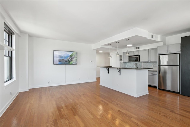 kitchen featuring pendant lighting, a breakfast bar, backsplash, gray cabinets, and appliances with stainless steel finishes