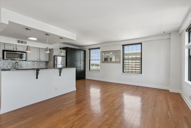 kitchen featuring hanging light fixtures, a breakfast bar area, gray cabinets, decorative backsplash, and appliances with stainless steel finishes