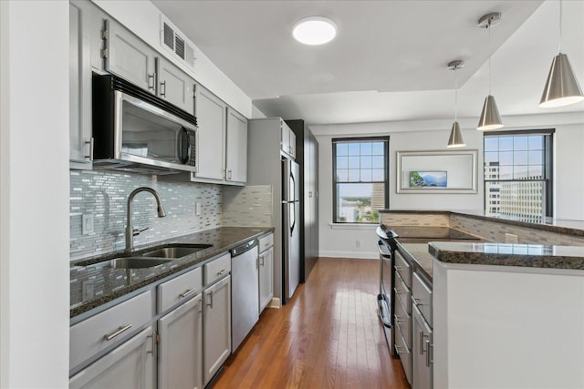 kitchen with appliances with stainless steel finishes, dark wood-type flooring, sink, pendant lighting, and gray cabinets