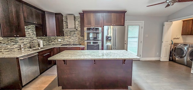 kitchen with sink, wall chimney exhaust hood, washer and dryer, a breakfast bar area, and stainless steel appliances