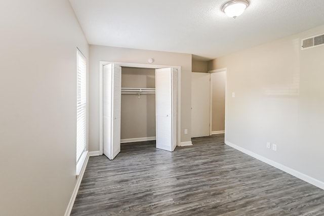 unfurnished bedroom featuring a textured ceiling, dark hardwood / wood-style flooring, and a closet