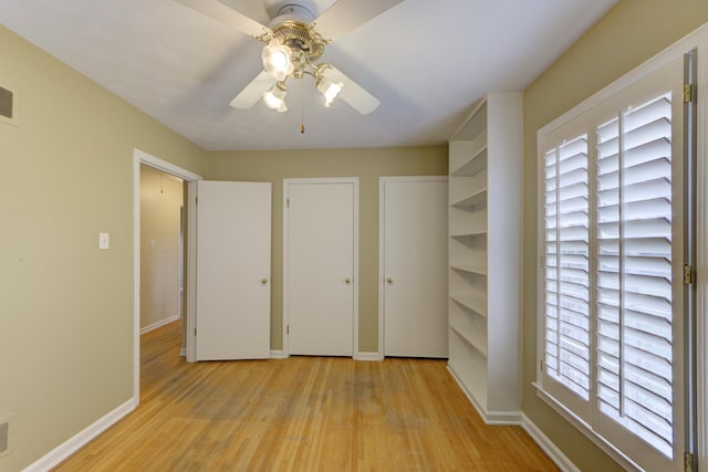 unfurnished bedroom featuring ceiling fan, light wood-type flooring, and two closets