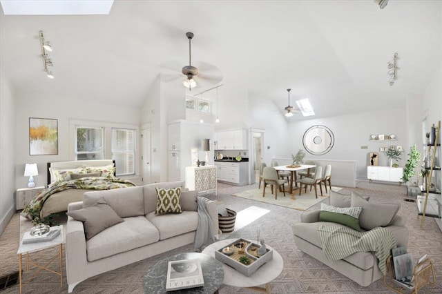 living room with ceiling fan, rail lighting, light colored carpet, and lofted ceiling with skylight