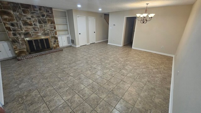 unfurnished living room with a stone fireplace, a notable chandelier, a textured ceiling, and built in shelves