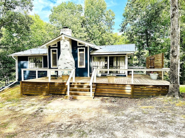 back of house with a deck, metal roof, and a chimney