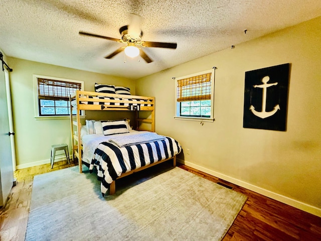 bedroom with ceiling fan, a textured ceiling, baseboards, and wood finished floors