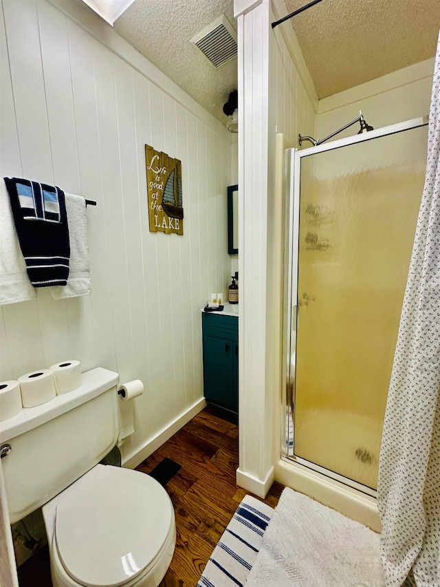 full bath with a textured ceiling, toilet, wood finished floors, visible vents, and a shower stall