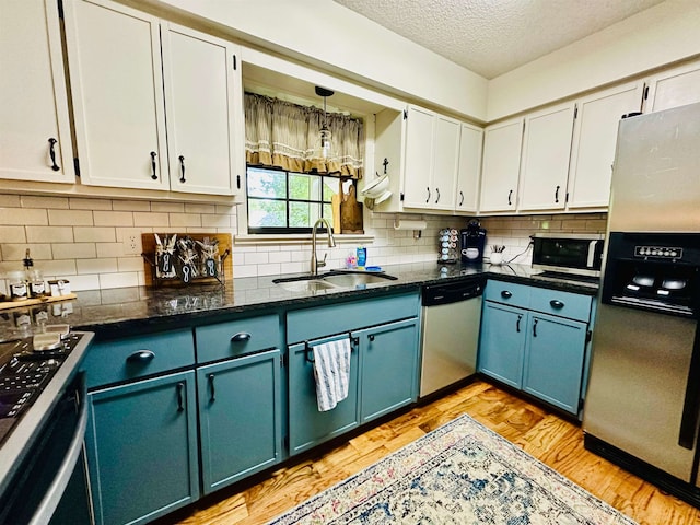 kitchen with appliances with stainless steel finishes, white cabinetry, a sink, and light wood finished floors