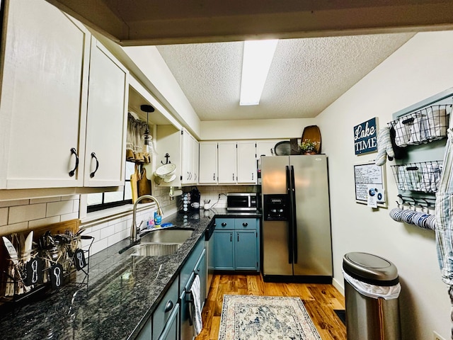 kitchen with light wood-style flooring, stainless steel appliances, a sink, white cabinets, and dark stone counters