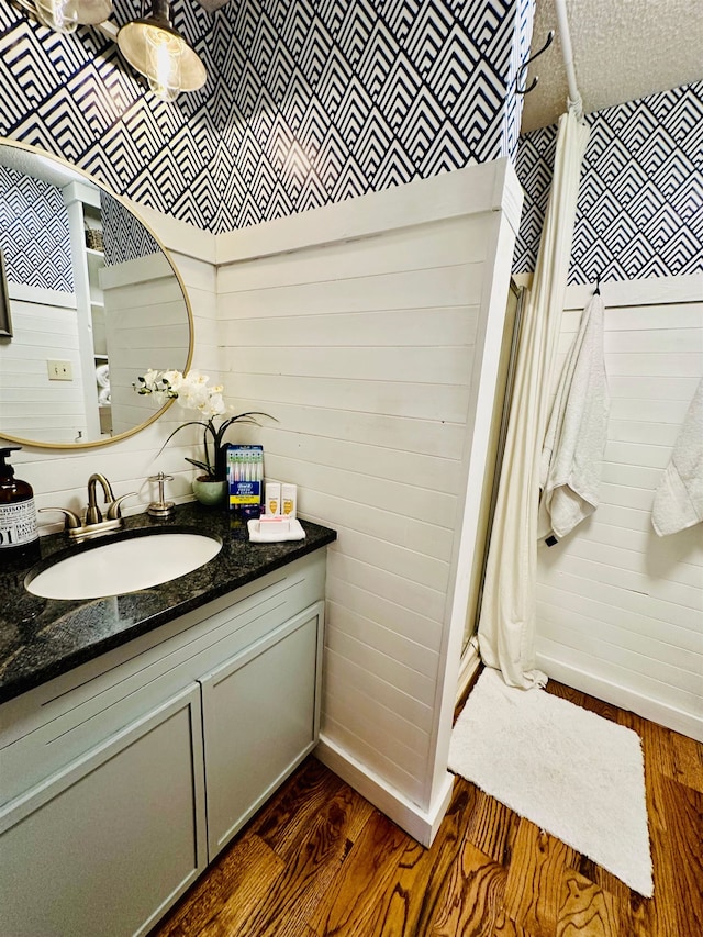 bathroom with wood walls, vanity, baseboards, and wood finished floors