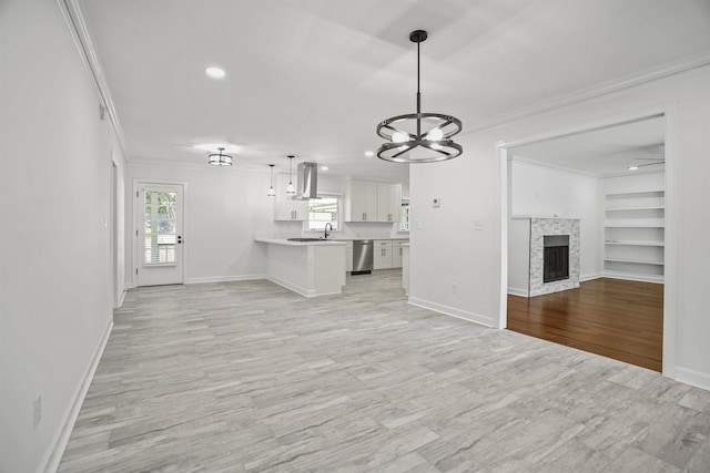 unfurnished living room featuring built in shelves, a stone fireplace, sink, ornamental molding, and light wood-type flooring