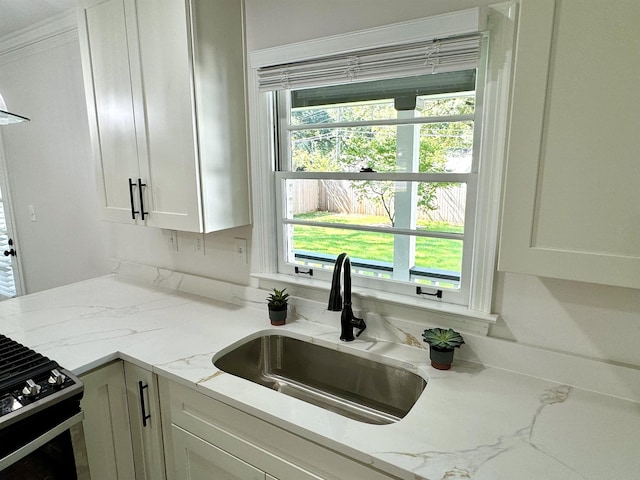 kitchen with light stone countertops, sink, white cabinetry, and gas range oven