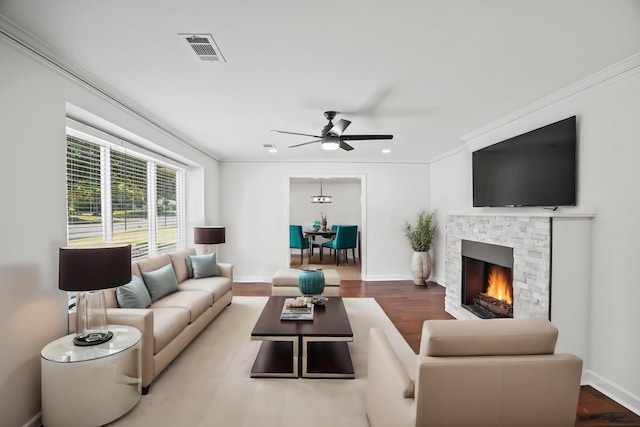 living room with ceiling fan, a stone fireplace, crown molding, and wood-type flooring