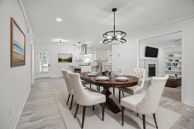 dining room with crown molding, sink, built in shelves, light hardwood / wood-style flooring, and an inviting chandelier