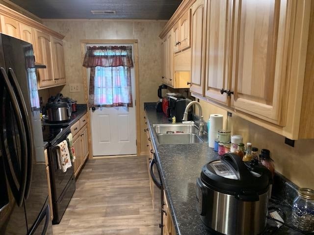 kitchen with dark stone counters, light hardwood / wood-style flooring, black appliances, sink, and light brown cabinets