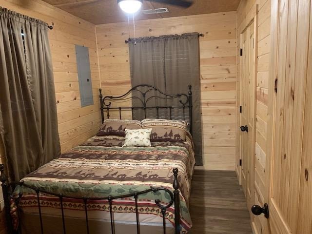 bedroom featuring hardwood / wood-style floors, electric panel, ceiling fan, and wooden walls