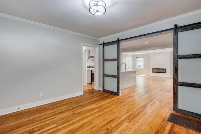 empty room with ornamental molding, light hardwood / wood-style flooring, and a barn door