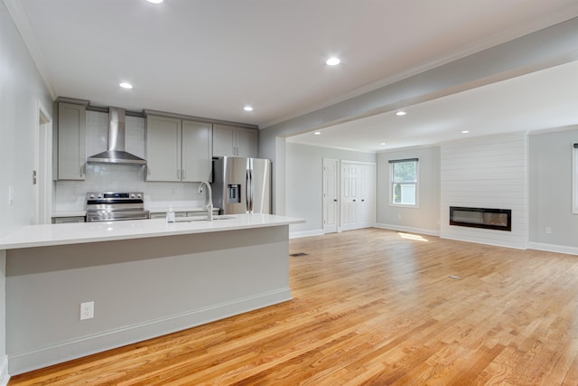 kitchen featuring backsplash, light hardwood / wood-style floors, appliances with stainless steel finishes, wall chimney exhaust hood, and a large fireplace