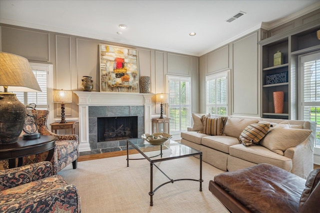 living room with a tiled fireplace, crown molding, and built in shelves