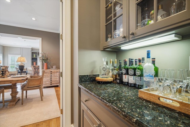 bar with crown molding, dark stone counters, and light hardwood / wood-style floors