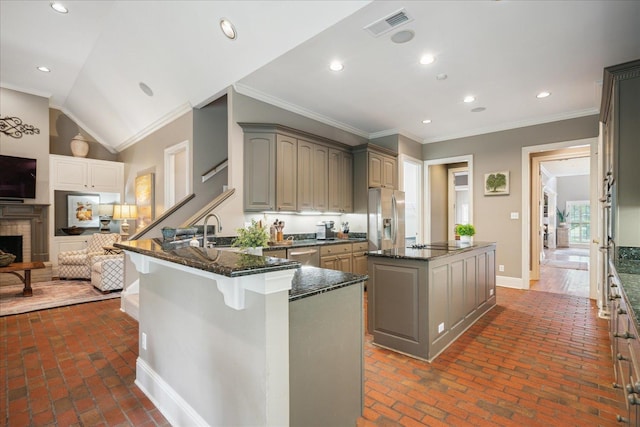 kitchen with appliances with stainless steel finishes, dark stone counters, vaulted ceiling, a kitchen island, and ornamental molding