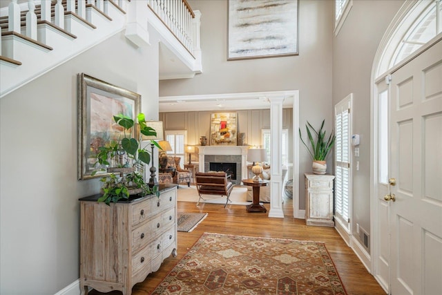 foyer with light hardwood / wood-style floors, a tile fireplace, decorative columns, and a high ceiling