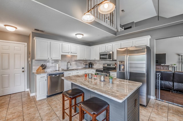 kitchen featuring sink, stainless steel appliances, light stone counters, white cabinets, and decorative light fixtures