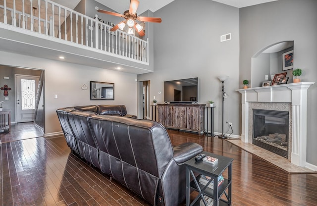 living room featuring a high ceiling, a premium fireplace, dark wood-type flooring, and ceiling fan