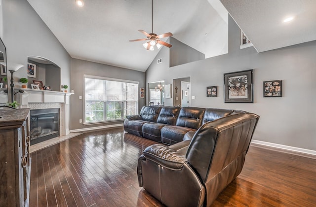 living room with dark wood-type flooring, ceiling fan, a premium fireplace, and high vaulted ceiling