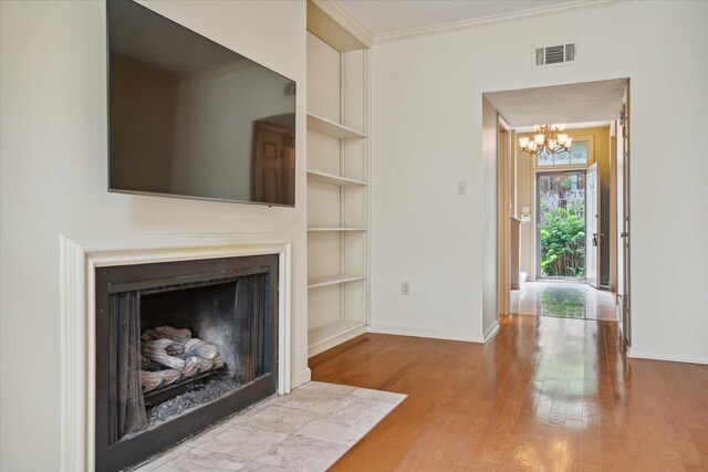 unfurnished living room with built in shelves, ornamental molding, light hardwood / wood-style floors, and an inviting chandelier