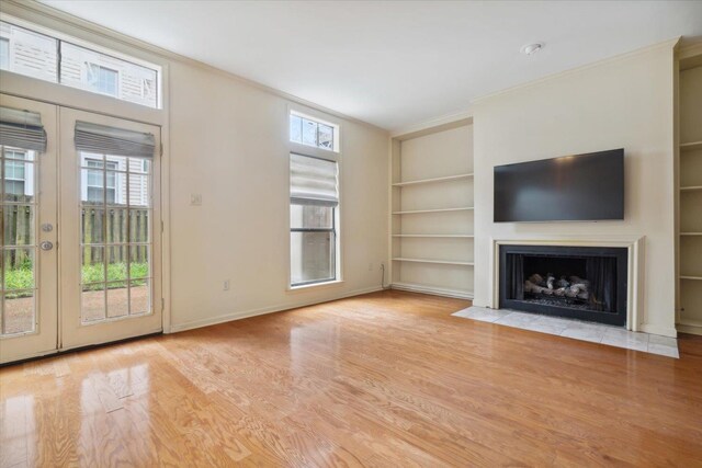 unfurnished living room featuring ornamental molding, built in features, light hardwood / wood-style flooring, and french doors