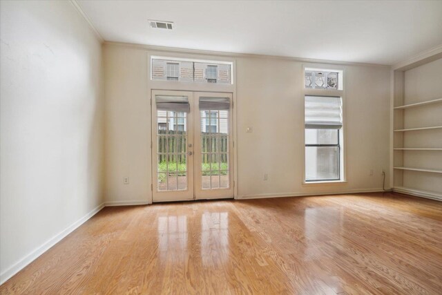 unfurnished room featuring light wood-type flooring, built in shelves, french doors, and ornamental molding