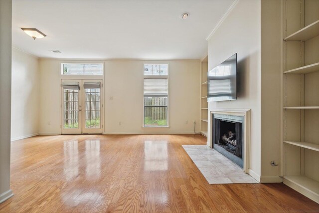 unfurnished living room with crown molding, a tile fireplace, light wood-type flooring, built in shelves, and french doors