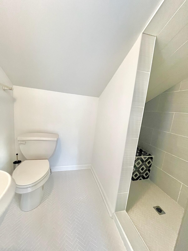 bathroom featuring vaulted ceiling, a tile shower, tile patterned floors, and toilet