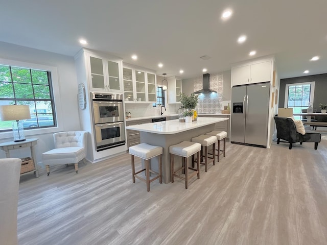 kitchen featuring wall chimney range hood, light hardwood / wood-style flooring, stainless steel appliances, white cabinets, and a kitchen island