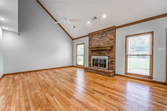 unfurnished living room with light wood-type flooring, ceiling fan, a brick fireplace, brick wall, and ornamental molding