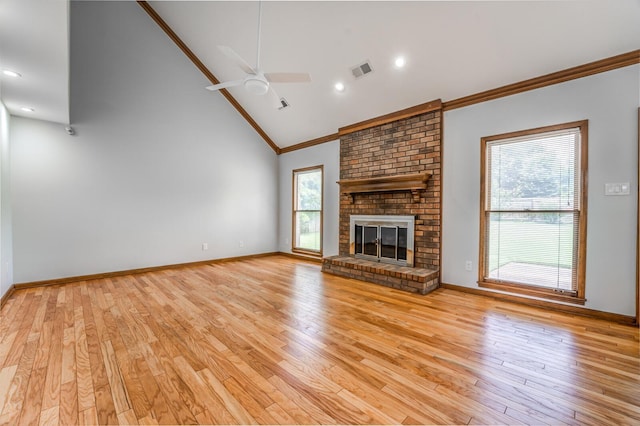 unfurnished living room featuring high vaulted ceiling, visible vents, a brick fireplace, light wood finished floors, and crown molding