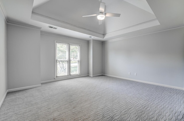 carpeted empty room featuring a tray ceiling, visible vents, crown molding, and baseboards