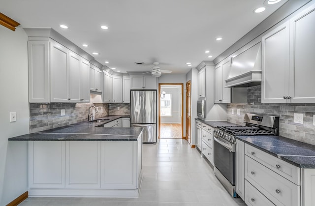 kitchen with appliances with stainless steel finishes, kitchen peninsula, light wood-type flooring, ceiling fan, and custom range hood