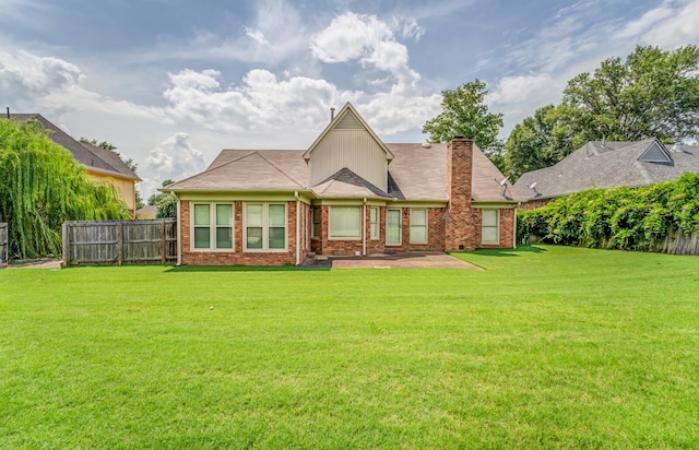 back of property with brick siding, a chimney, fence, and a lawn