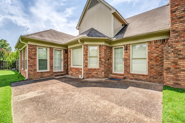 exterior space featuring brick siding, a shingled roof, a front lawn, and a patio