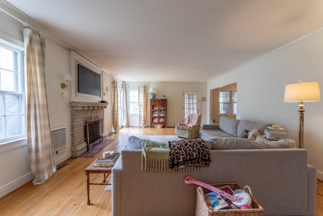 living room with ornamental molding, light hardwood / wood-style flooring, a healthy amount of sunlight, and a brick fireplace