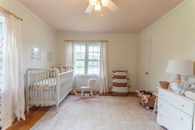 bedroom with a crib, ceiling fan, crown molding, and light hardwood / wood-style flooring