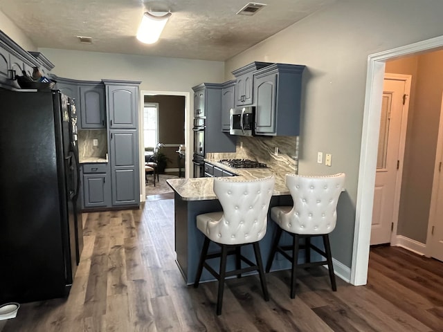 kitchen featuring hardwood / wood-style floors, a kitchen bar, appliances with stainless steel finishes, kitchen peninsula, and backsplash