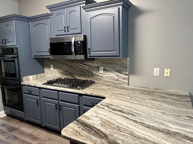 kitchen with stainless steel appliances, gray cabinetry, backsplash, light stone countertops, and dark wood-type flooring