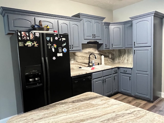 kitchen featuring black appliances, light stone countertops, hardwood / wood-style floors, decorative backsplash, and sink