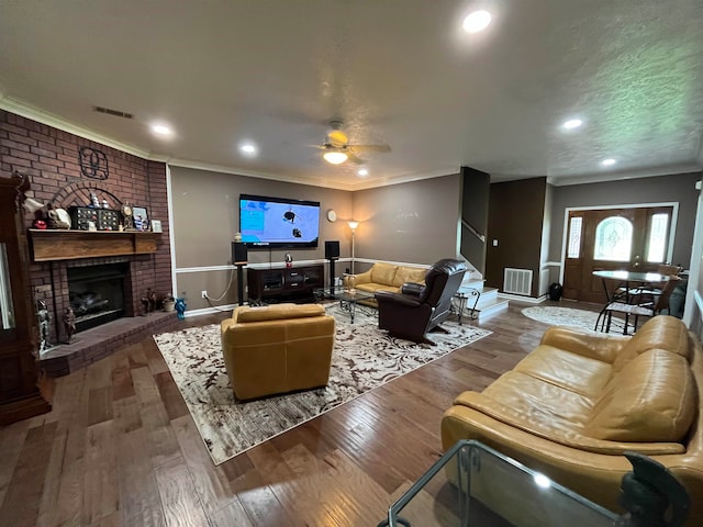 living room featuring ceiling fan, a brick fireplace, wood-type flooring, and ornamental molding