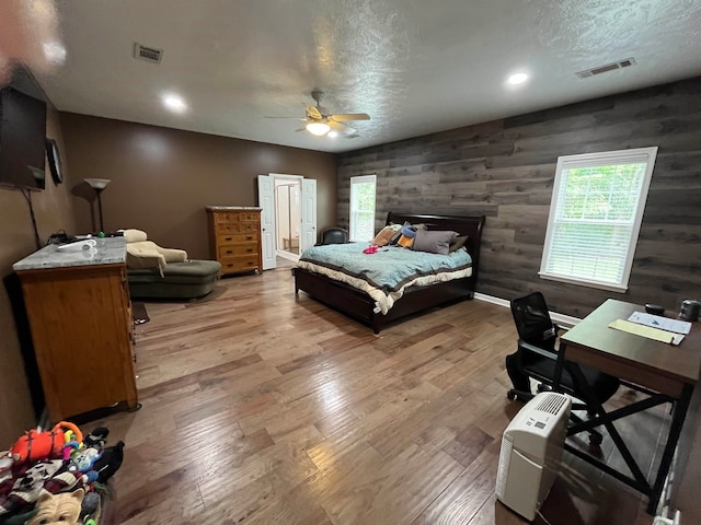 bedroom with wood walls, a textured ceiling, hardwood / wood-style flooring, and ceiling fan