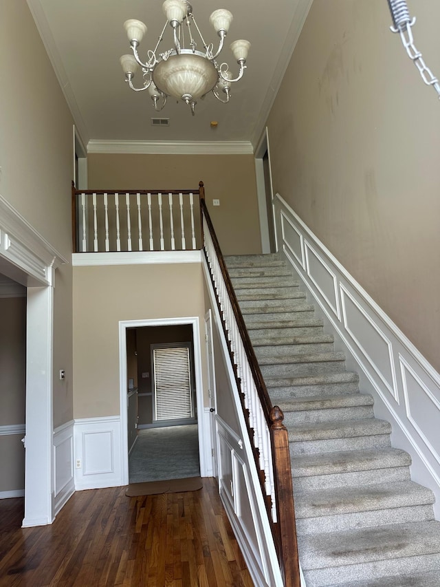 staircase featuring wood-type flooring, ornamental molding, and a chandelier